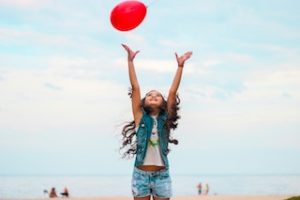 ребенок на пляже ловит воздушный красный шар